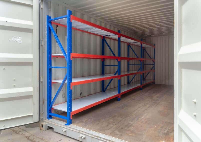 Empty industrial metal shelving unit with blue frame and red supports inside a shipping container
