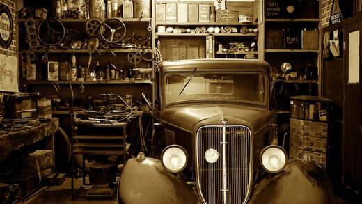 Vintage sepia photo of an old car in a cluttered classic garage with tools and equipment