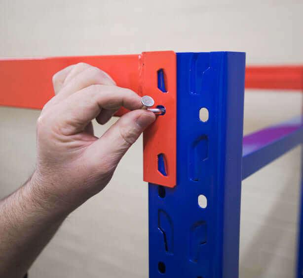 Hand tightening bolt on blue and red metal shelving unit in a warehouse or storage area